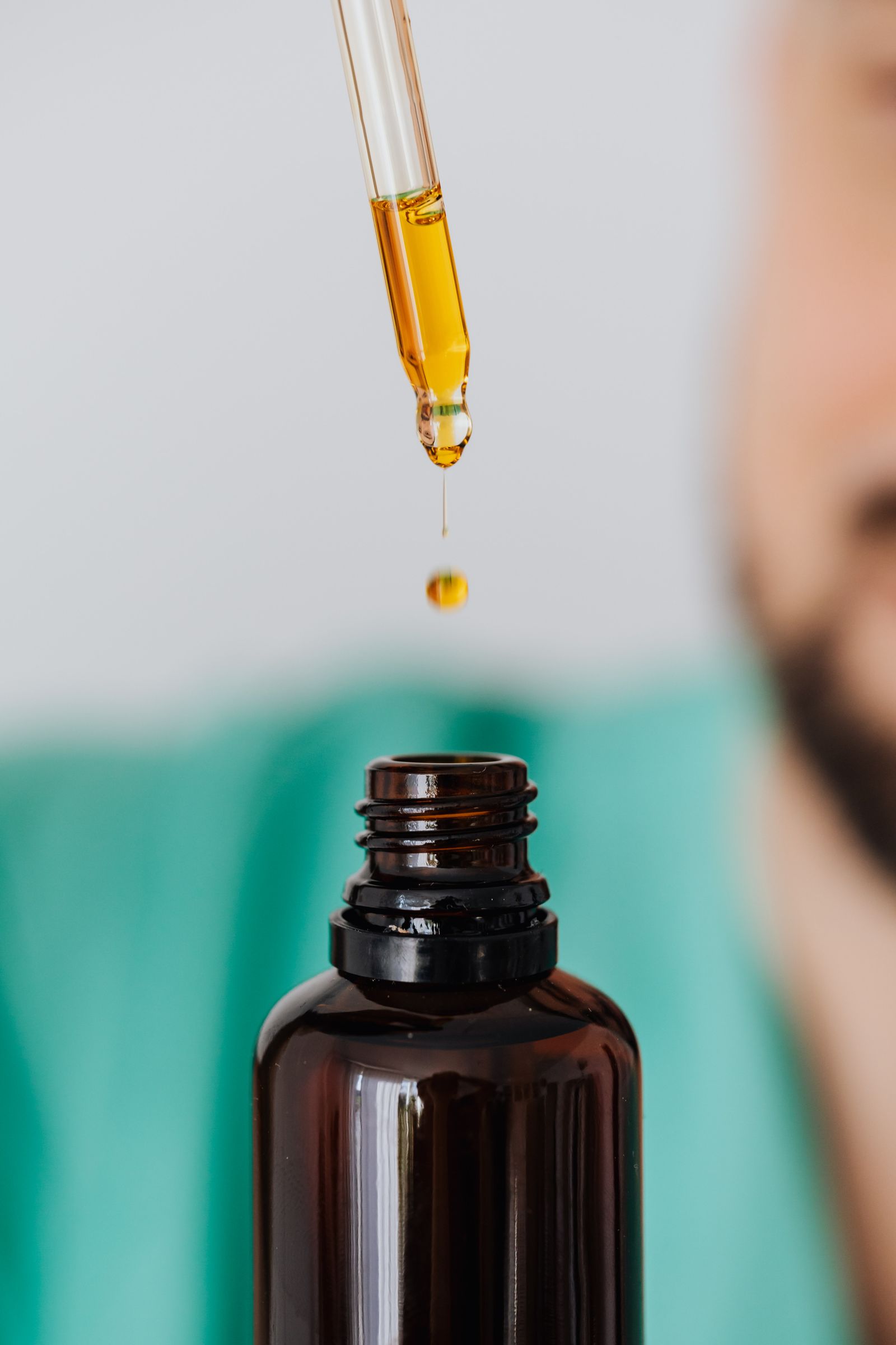 Golden oil held in a glass dropper above an amber bottle